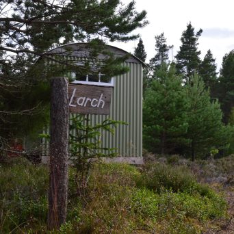 a sign over a grassy area with trees in the background